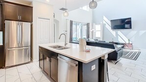 Una cocina moderna con electrodomésticos de acero inoxidable, una isla central y un comedor con sofá y televisor.