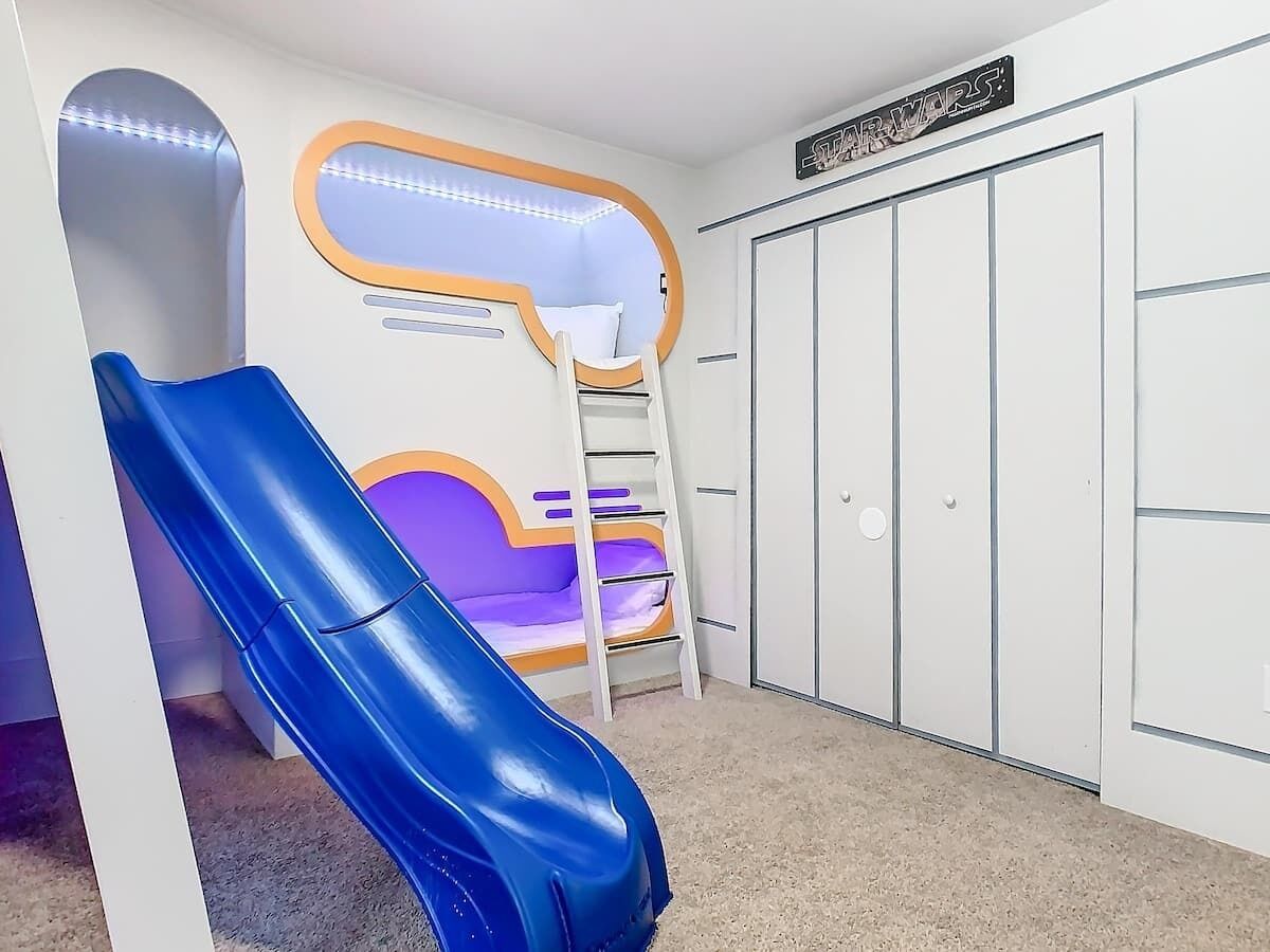 Un espace de jeux pour enfants avec un toboggan bleu, un mur d’escalade violet et une échelle blanche.