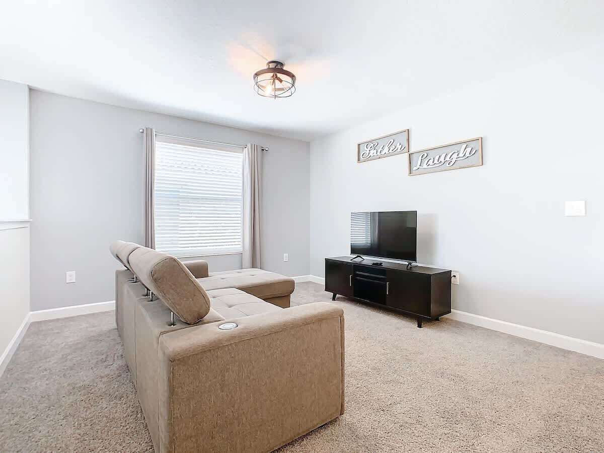 A living room with a beige sofa, a TV on a black stand, and two wall decorations with the words "Laugh" and "Laugh".