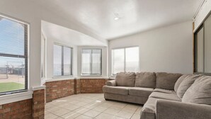A living room with a brick wall, a grey sectional sofa, and large windows with blinds. - 4BR Glendale Ranch - Family & Horse Friendly! (Glendale)