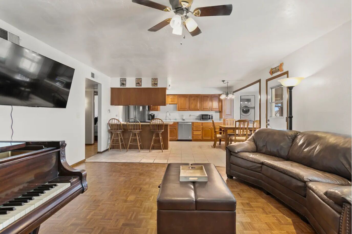 A living room with a piano, a leather sofa, and a dining area with wooden chairs.
