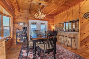 A wooden cabin interior with a dining area, kitchen, and bar. - Hawk's Rest: Private Cabin, Great Views, Hot Tub, WIFI, Fireplace (Ferguson)