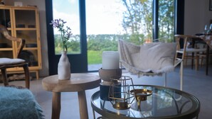 Una habitación acogedora con una mesa redonda de cristal, un jarrón blanco con flores, una vela y un pequeño farol.