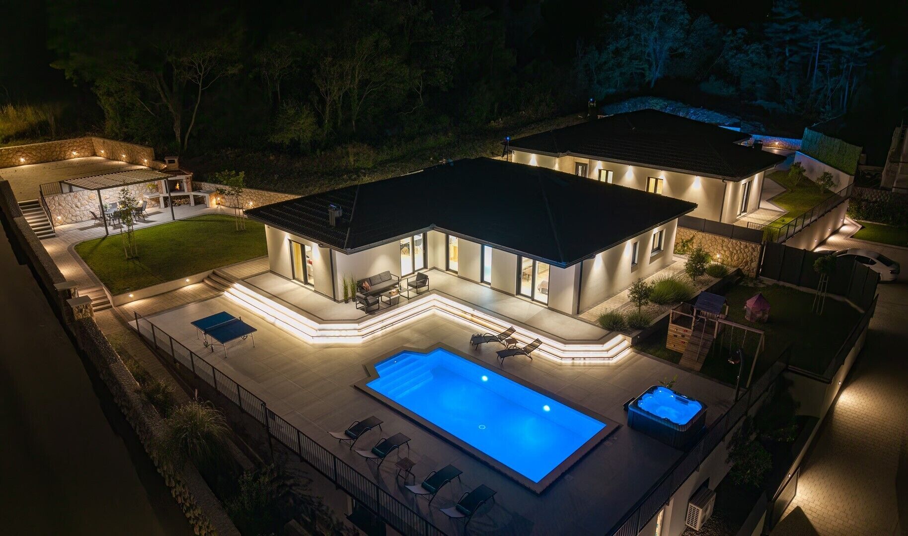 Een modern huis met een zwembad, terrasmeubels buiten en een goed verlicht terras.