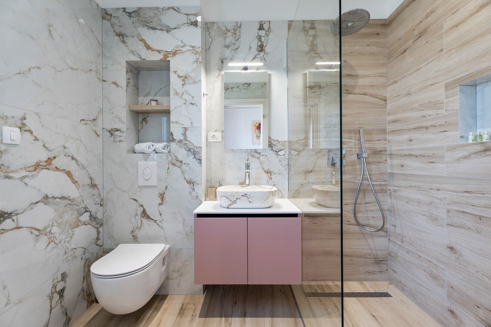 Une salle de bain moderne avec des murs en marbre, une douche en verre et un meuble-lavabo rose.