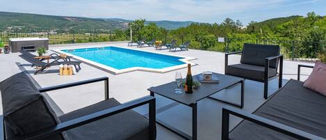 A rooftop terrace with a swimming pool, outdoor furniture, and a scenic view of the countryside.