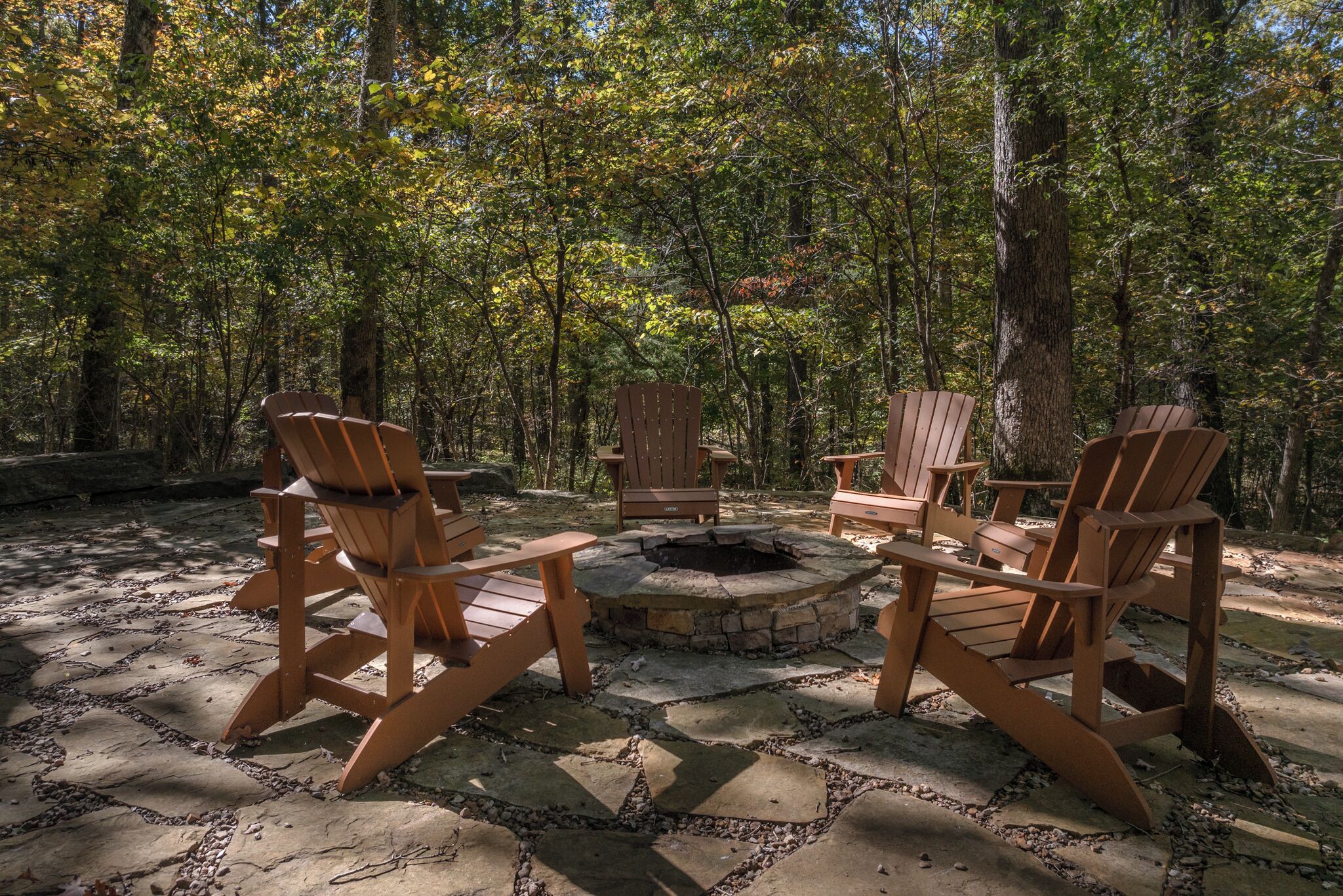 Un foyer entouré de fauteuils Adirondack, le tout situé dans un cadre forestier.