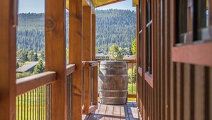 A wooden balcony with a stone barrel, wooden railings, and a view of a forested mountain. - Enchanting Home! 10 Min Drive to Resort, 5 Min to Town Center! (Big Sky)