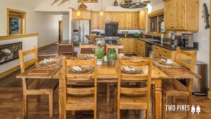 A spacious kitchen with wooden cabinets, a dining table set for six, and a large island. - Enchanting Home! 10 Min Drive to Resort, 5 Min to Town Center! (Big Sky)