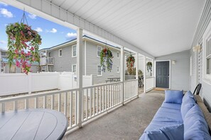 A covered porch with a white railing, a round table, and a sofa.