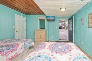 A room with two beds, a wooden ceiling, a white door, a dresser, and a television on the wall.