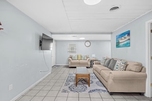 Una sala de estar con un sofá color beige, una mesa de centro, un televisor montado en la pared y un cuadro de un barco.