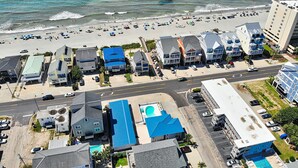 Une vue aérienne d’une zone côtière avec une plage, une piscine et plusieurs bâtiments.