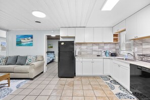 A modern kitchen with white cabinets, a black refrigerator, and a coffee maker.
