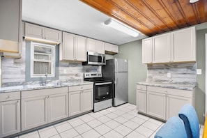 Una cocina compacta con armarios blancos, microondas, refrigerador y estufa.