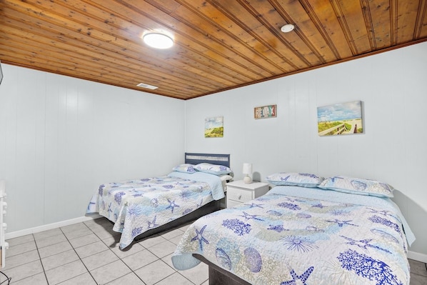 A bedroom with two beds, white walls, wooden ceiling, and artwork on the walls.