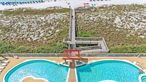 A pool area with two large pools, a wooden deck, and a lifeguard stand. - Gulf Front Condo | Pearl of Navarre 702 | Panoramic Views, Resort Amenities (Navarre Beach)