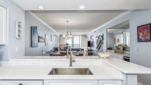 A modern kitchen with a central island, a built-in dishwasher, and a large window overlooking a dining area. - Gulf Front Condo | Pearl of Navarre 702 | Panoramic Views, Resort Amenities (Navarre Beach)