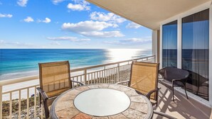 A balcony with a round table and two chairs, overlooking a beach and ocean. - Gulf Front Condo | Pearl of Navarre 702 | Panoramic Views, Resort Amenities (Navarre Beach)