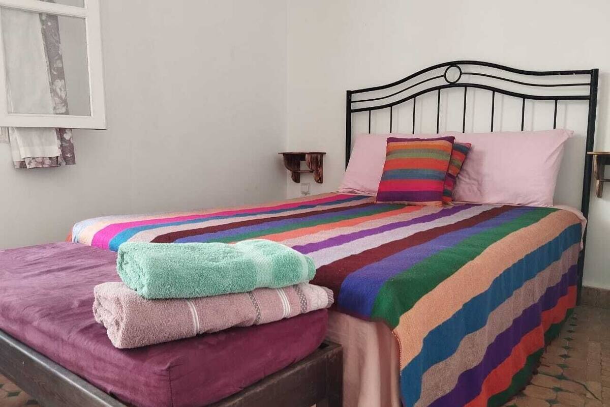 A bed with a colorful striped blanket, a pink pillow, and a green towel on the side.