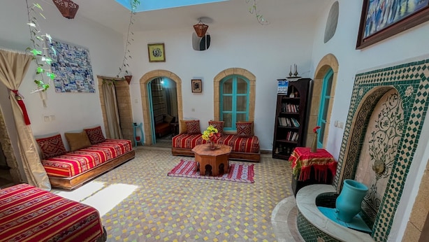A cozy living room with patterned flooring, two sofas with red cushions, a coffee table, and a bookshelf. - Riad Darko  (Essaouira)