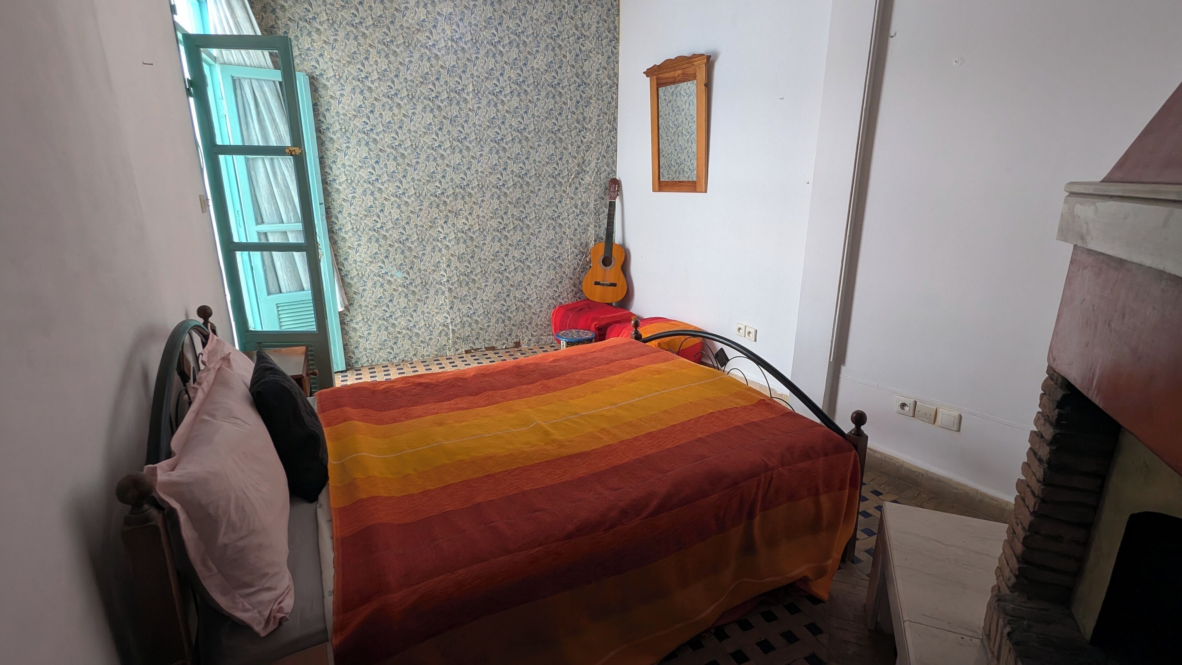 A small, cozy bedroom with a bed, a guitar, and a red suitcase.