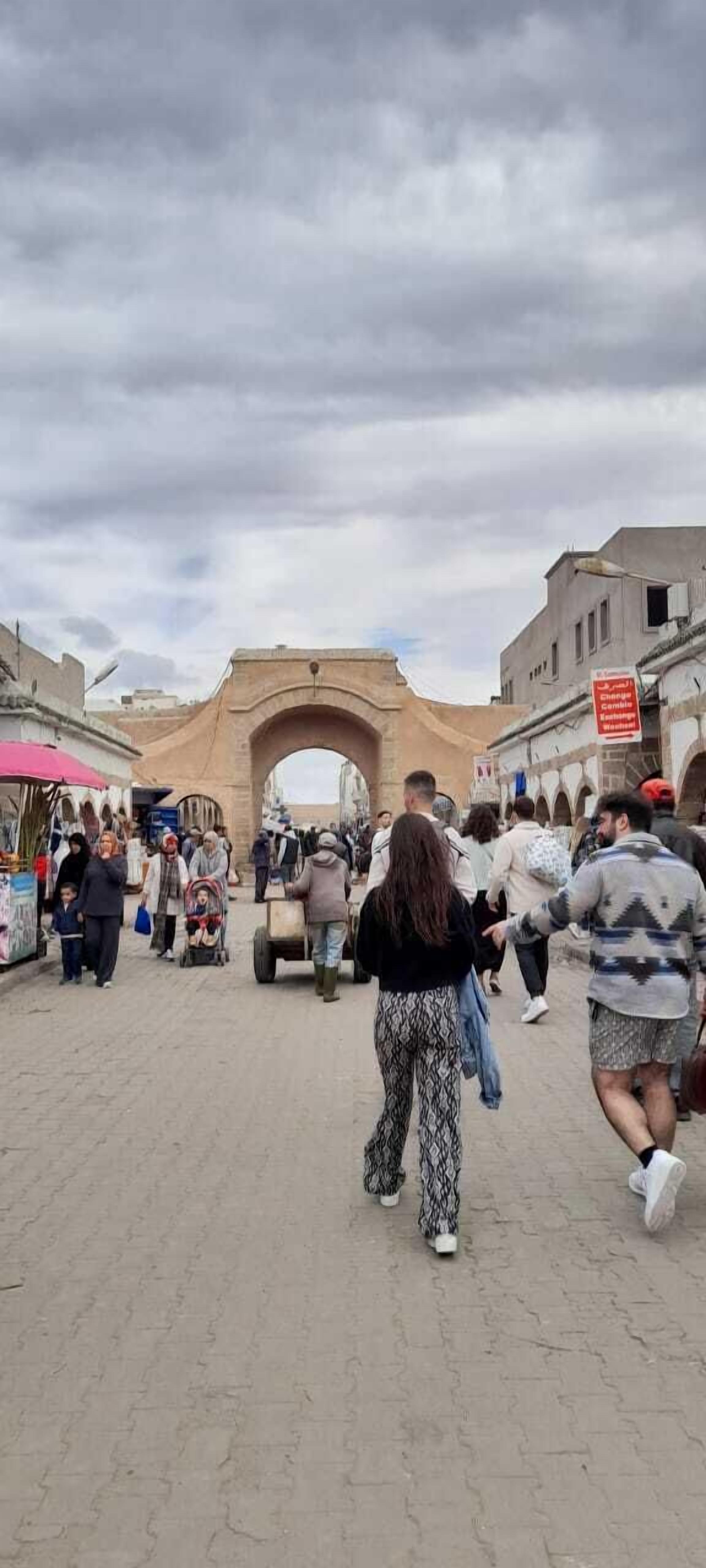 A bustling street scene with an archway, market stalls, and people walking.