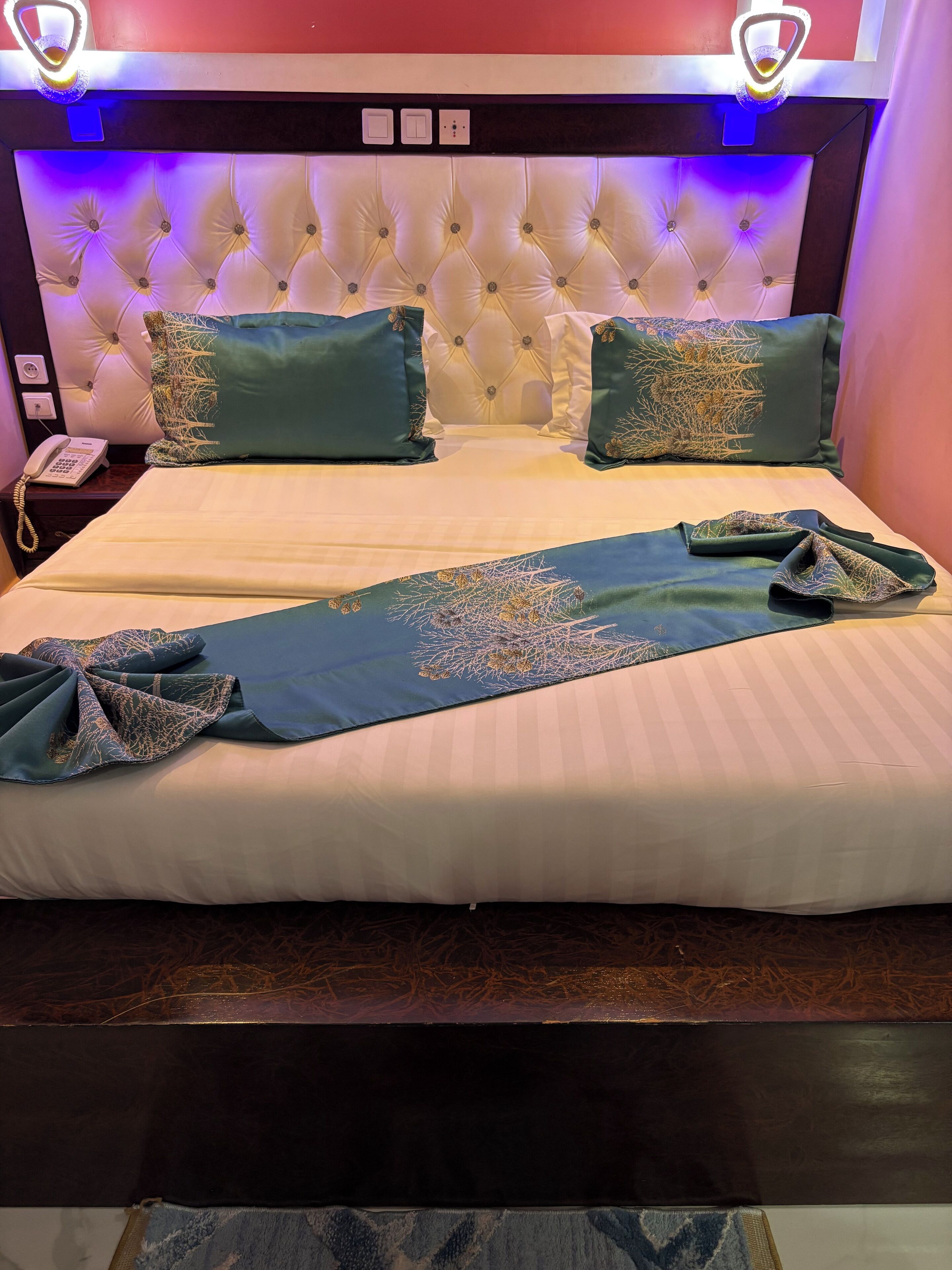 Un letto ordinato con testiera trapuntata, due cuscini decorativi e una coperta ripiegata.