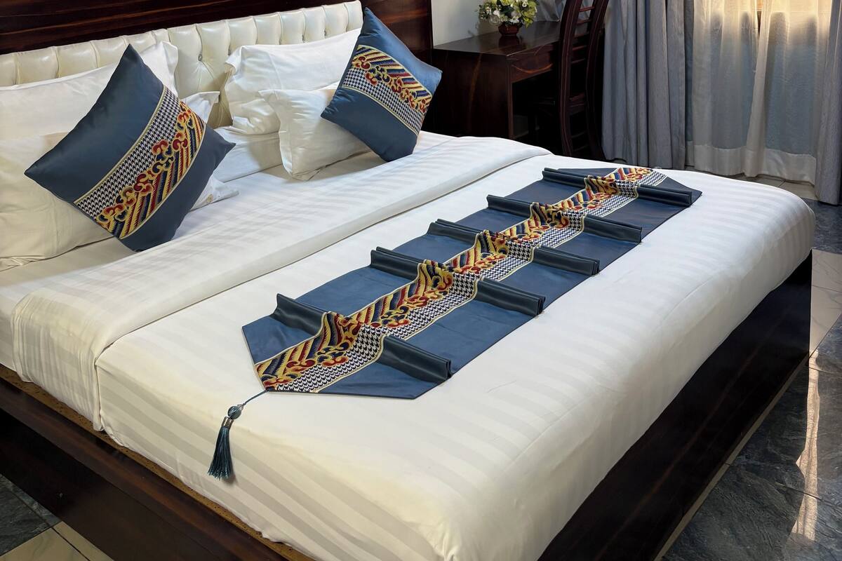 A hotel room with a neatly made bed, a nightstand with a vase of flowers, and a painting on the wall.