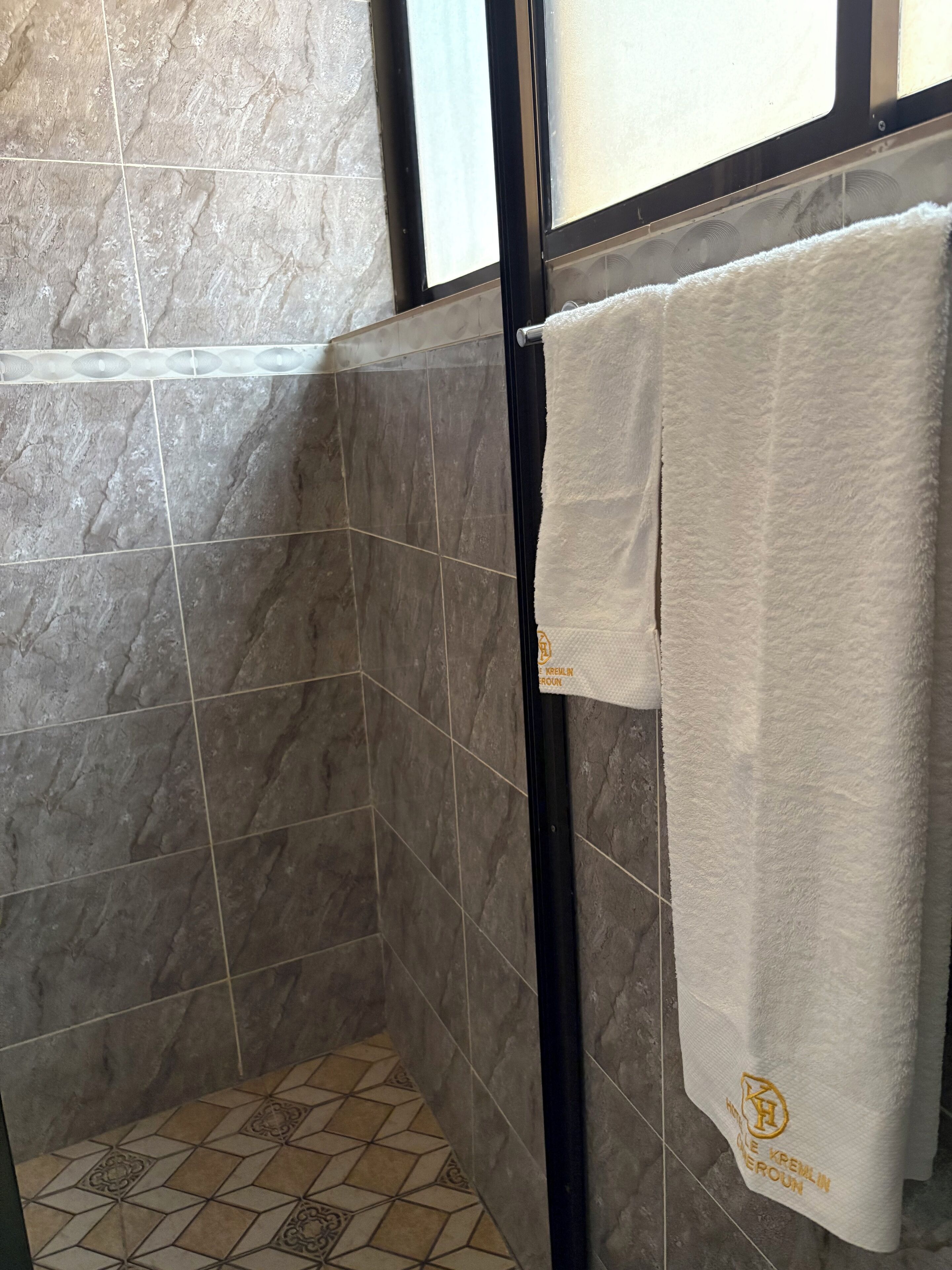 A bathroom with grey marble tiles, a shower area, and a towel hanging on a rack.