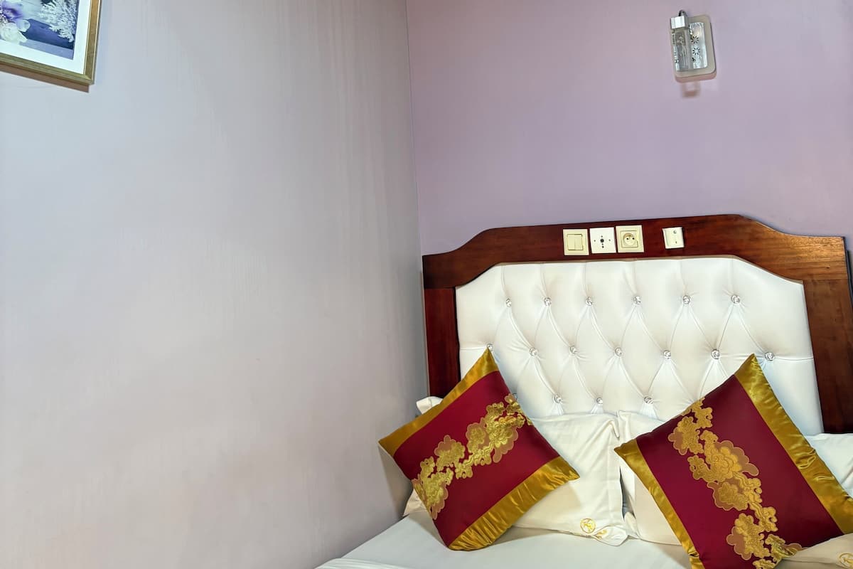 A bedroom with a wooden ceiling, a bed with white bedding and two red pillows with gold designs, and a framed picture on the wall.