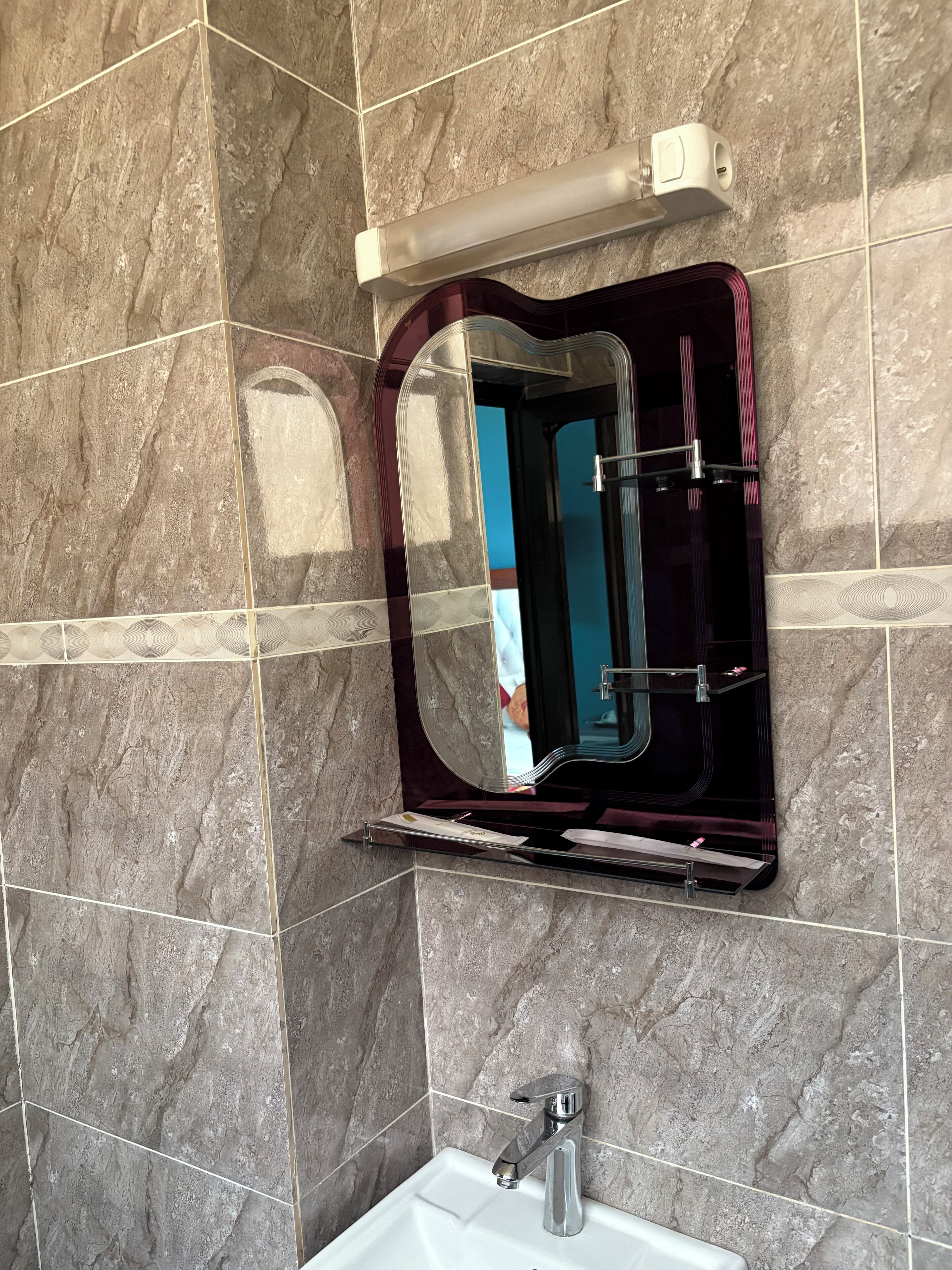 A bathroom with a marble wall, a vanity with a mirror, and a sink.