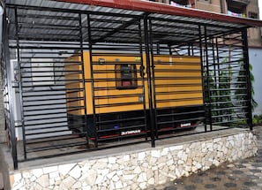 A yellow vehicle with "ALBA" and "D40P3" on the side, parked under a metal structure with a stone base. - HOTEL LE KREMLIN (Yaoundé)