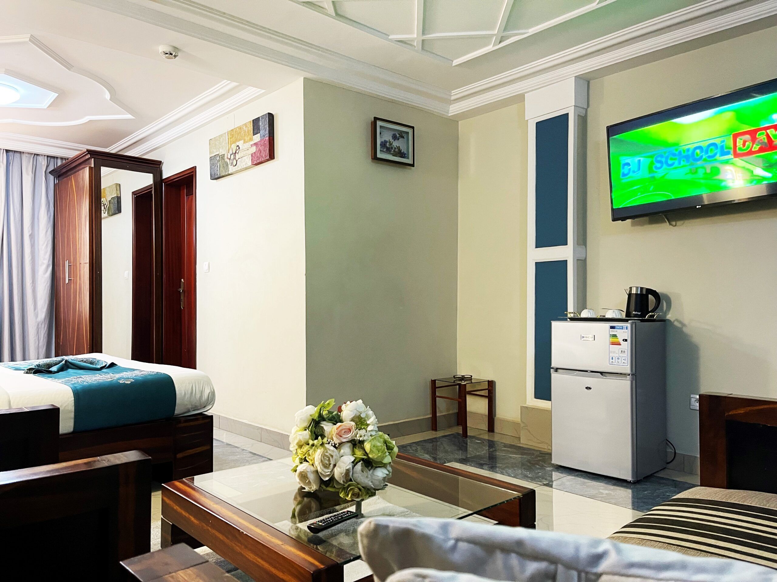Une chambre d’hôtel avec un lit, une machine à café, une télévision et une petite table sur laquelle est posé un vase de fleurs.