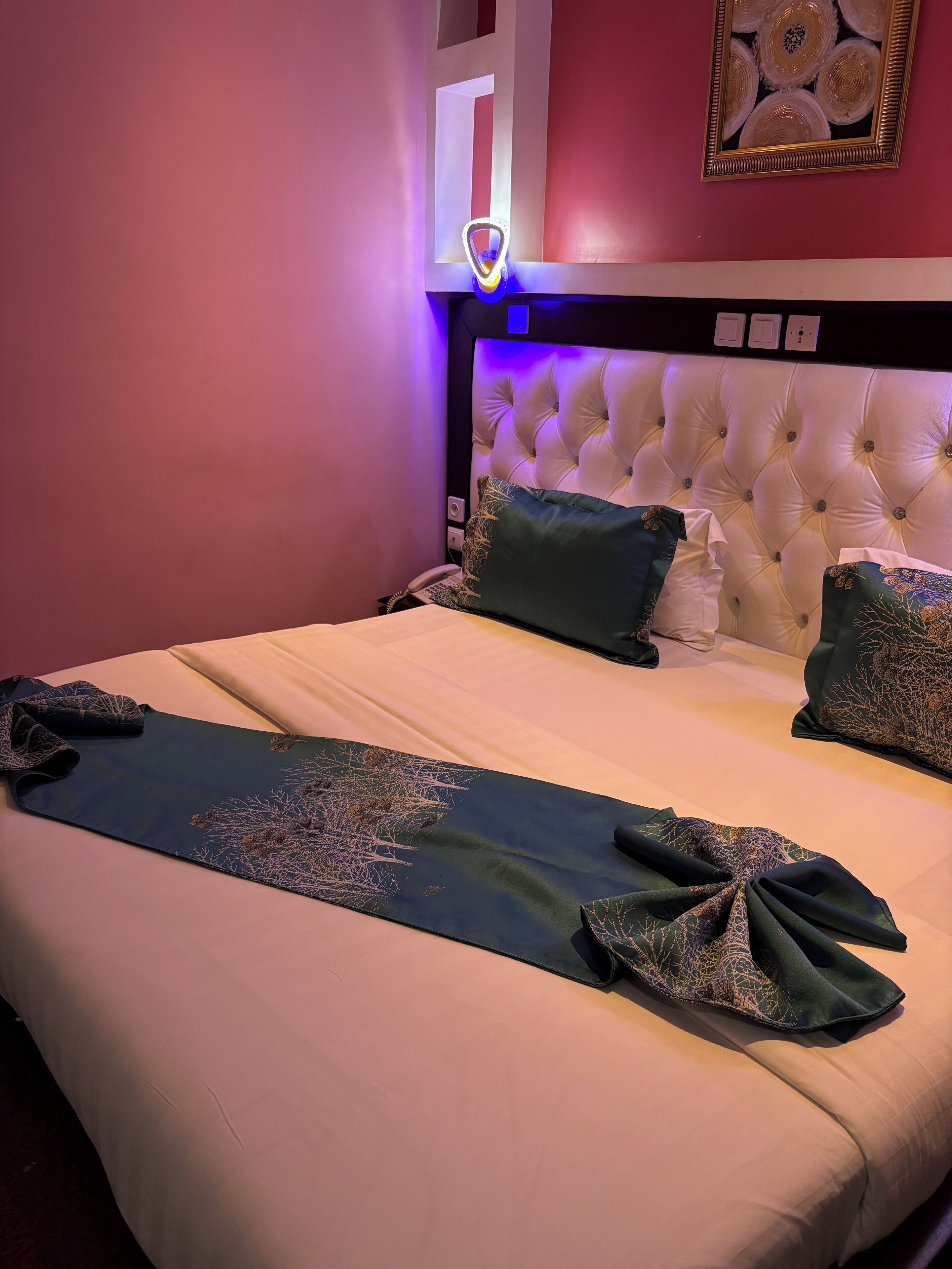 A neatly made bed with a decorative runner, a tufted headboard, and a bedside telephone.