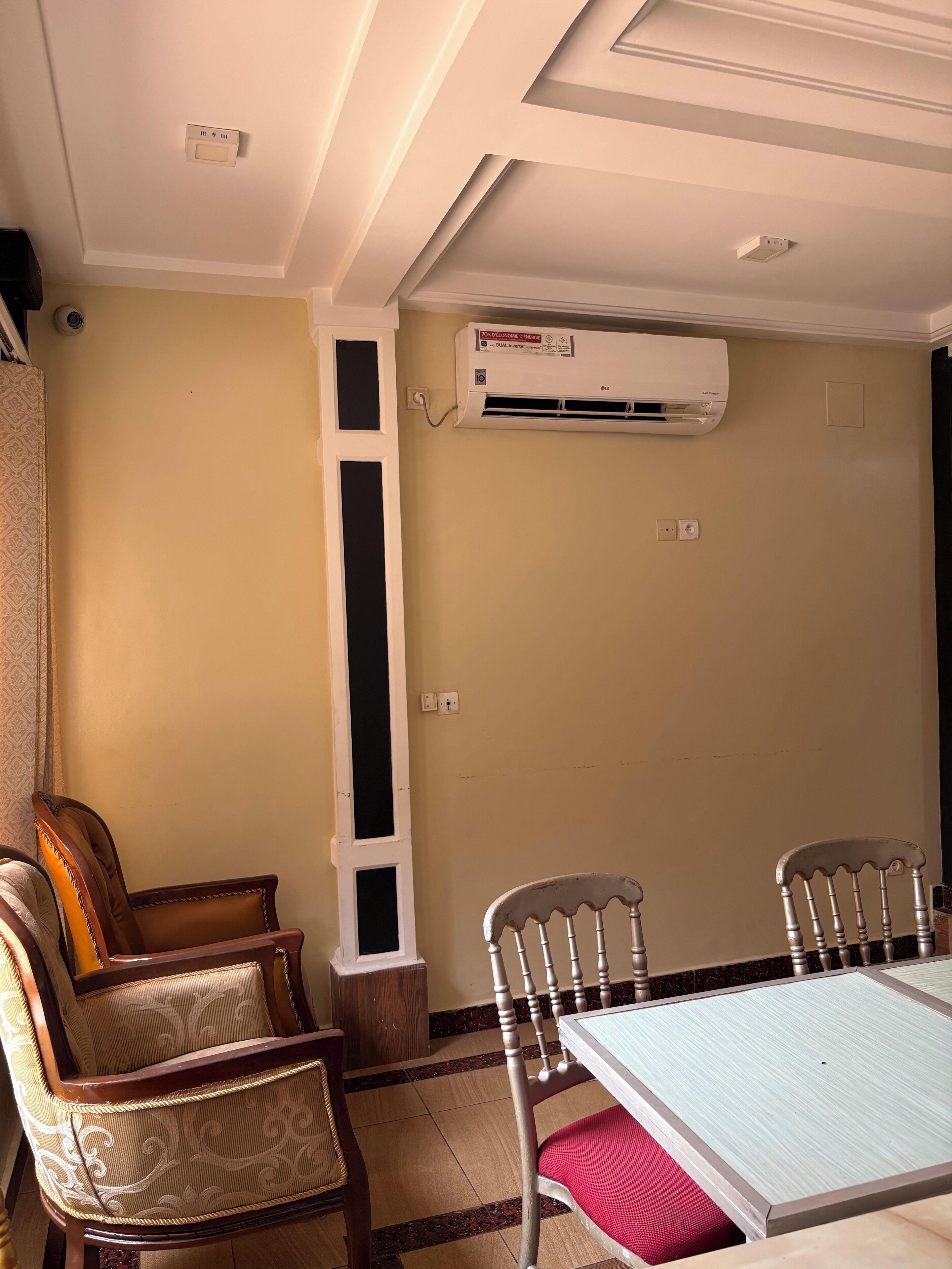 Un coin repas avec une table et des chaises, un climatiseur fixé au mur, et un rideau à motifs sur le côté gauche.