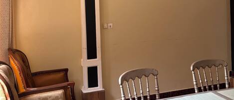 Un coin repas avec une table et des chaises, un climatiseur fixé au mur, et un rideau à motifs sur le côté gauche.