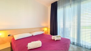 A hotel room with a bed, two pillows, a nightstand, a lamp, and a window with curtains. - Il Giardino Delle Farfalle by Ca-sa Check (Chioggia)