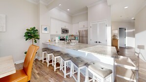 Una cocina moderna con armarios blancos, electrodomésticos de acero inoxidable y una isla de mármol con taburetes de bar.