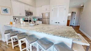 A kitchen with a large island, bar stools, stainless steel appliances, and white cabinetry.