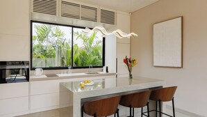 A modern kitchen with a large window, a central island with bar stools, and a decorative light fixture. - SOLAIR Pererenan Loft #9 - 1 bdr - with pool and rooftop barbeque (Badung)