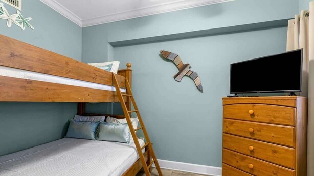 A room with a bunk bed, a wooden dresser, a television, and a wall decoration.