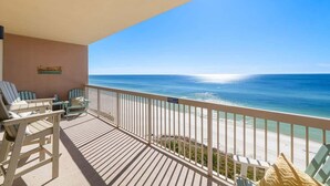 A balcony with a view of the ocean, featuring a wooden deck and several chairs.