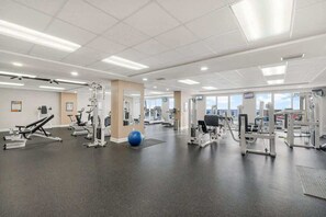Ein Fitnessstudio mit verschiedenen Trainingsgeräten, einem blauen Übungsball und einem großen Fenster, das für natürliches Licht sorgt.