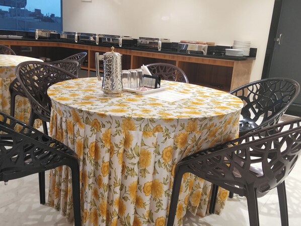 Een ronde tafel met een tafelkleed met bloemen, omringd door zwarte stoelen met gedetailleerde decoraties.