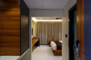 A modern hotel room with a bed, two chairs, a desk, and a ceiling fan.