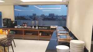 A modern kitchen with a large window overlooking a cityscape, equipped with a coffee machine, tea station, and ample storage. - Hotel Lemon Park (Visakhapatnam)