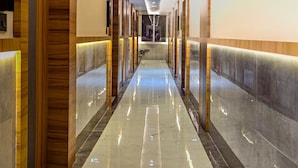 A hotel corridor with a polished marble floor, wooden paneling on the walls, and a series of doors on one side. - Hotel Lemon Park (Visakhapatnam)