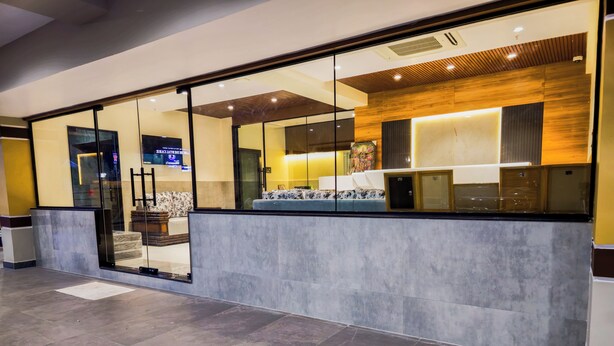A modern reception area with a glass partition, a seating area with patterned cushions, and a wooden accent wall. - Hotel Lemon Park (Visakhapatnam)