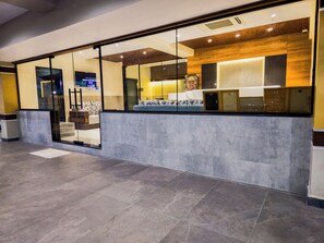 A modern reception area with a glass partition, a seating area with patterned cushions, and a wooden accent wall. - Hotel Lemon Park (Visakhapatnam)